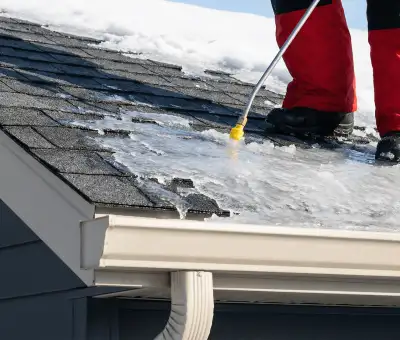 Ice dam removal technician using a steam wand to melt thick ice buildup on a residential roof in Fort Wayne, IN