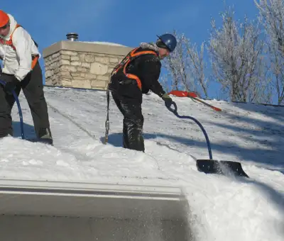 Professional technicians performing roof snow removal with safety harnesses and shovels in Fort Wayne, IN